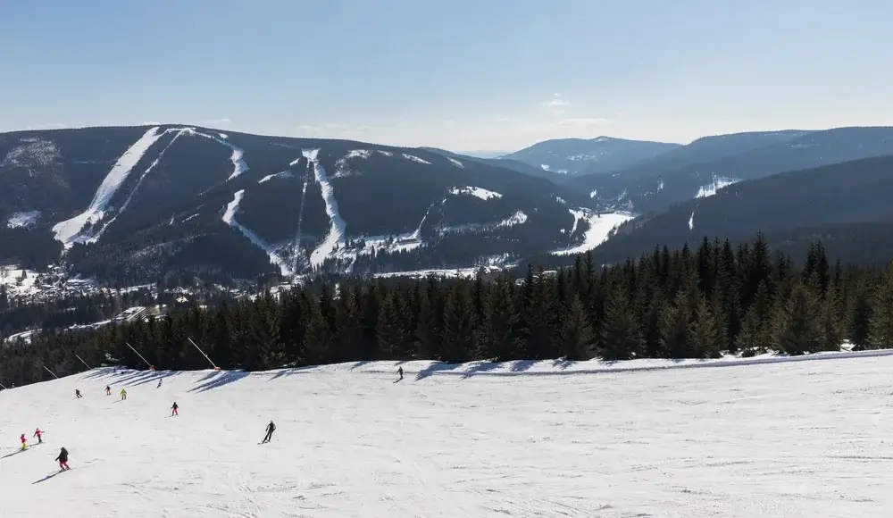 Skiløbere på bred nedfart i Spindleruv Mlyn med udsigt til flere pister i dalen